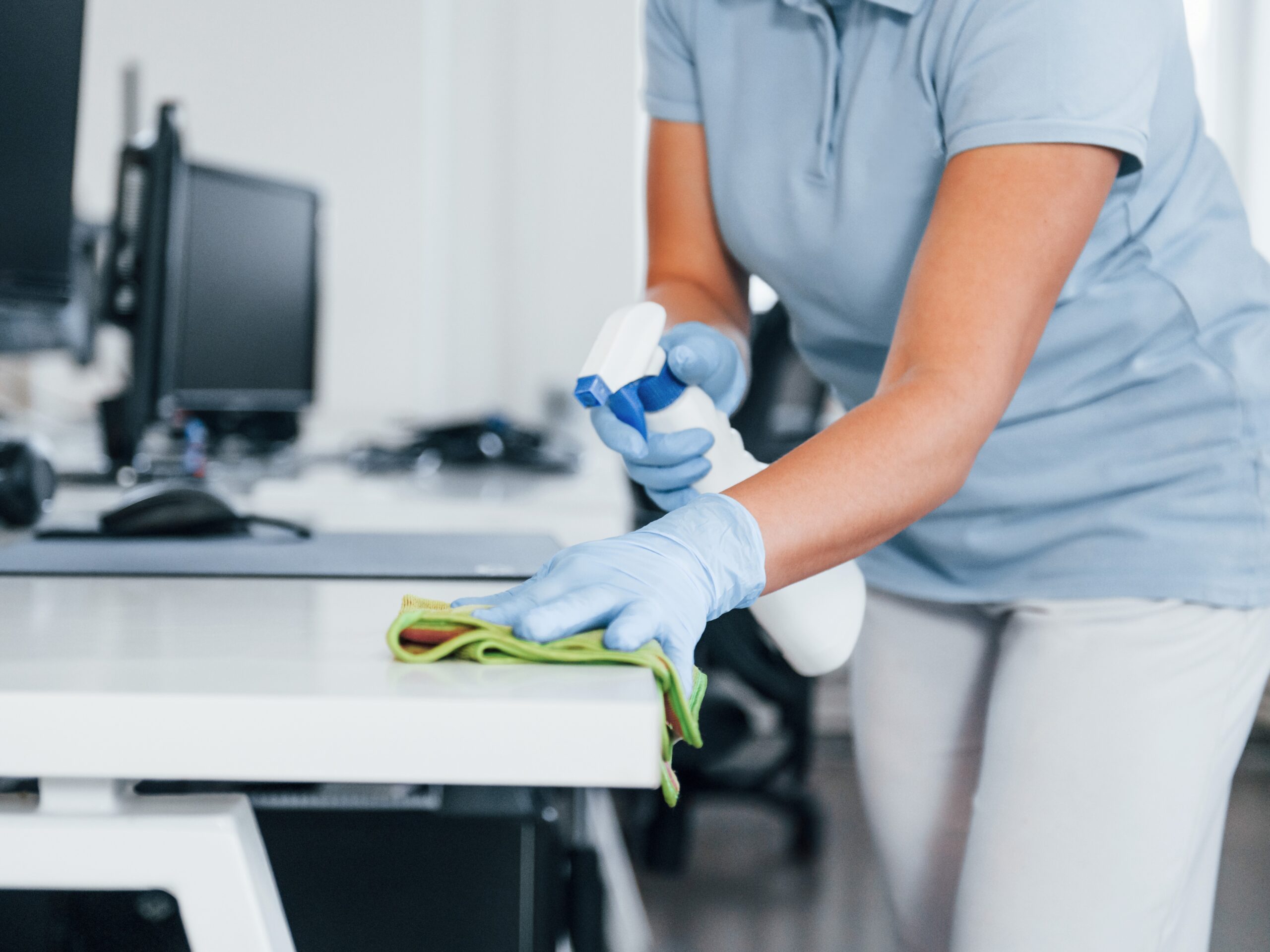 Close up view of woman in protective gloves that cleaning tables in the office.