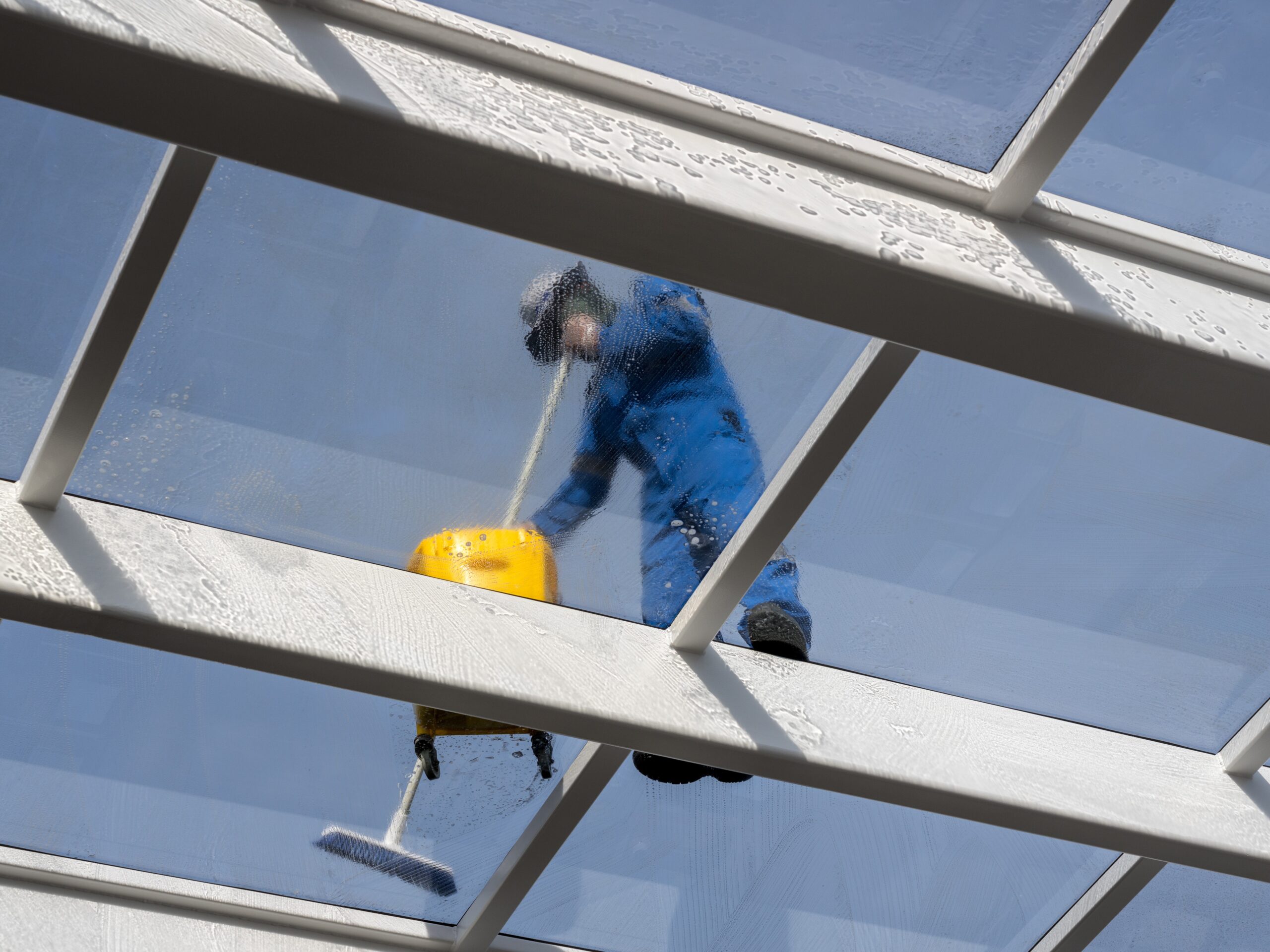 Male worker washing large expanse of glass roof over swimming pool